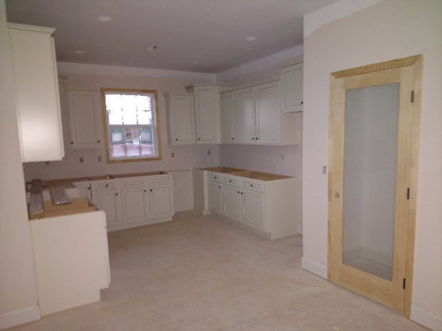 White kitchen cabinets with silver handles, glass door leading outside, white tile floor, white walls, and a large window with a white frame.