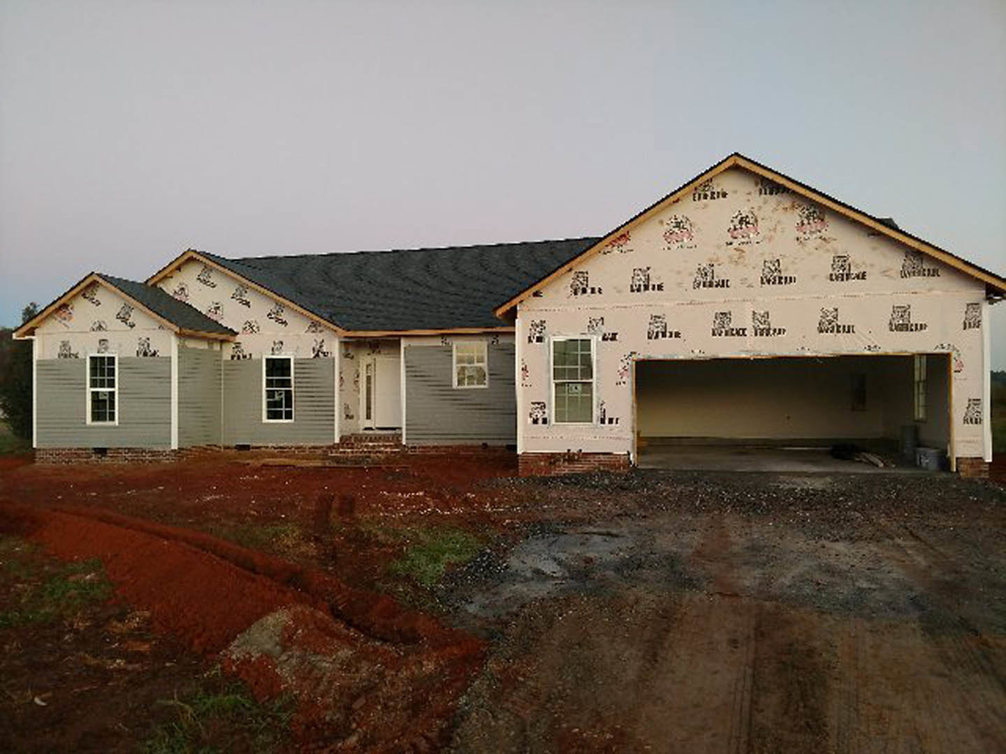 Two-story house with black roof, white-framed windows, attached garage with paneled door, light-colored siding, and paved driveway leading to entrance
