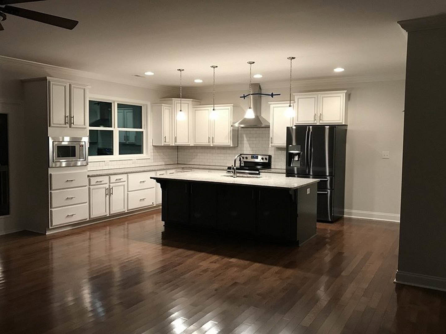 Spacious kitchen featuring a large quartz island, stainless steel appliances including microwave and black refrigerator, white cabinetry, modern faucet, and pendant lighting