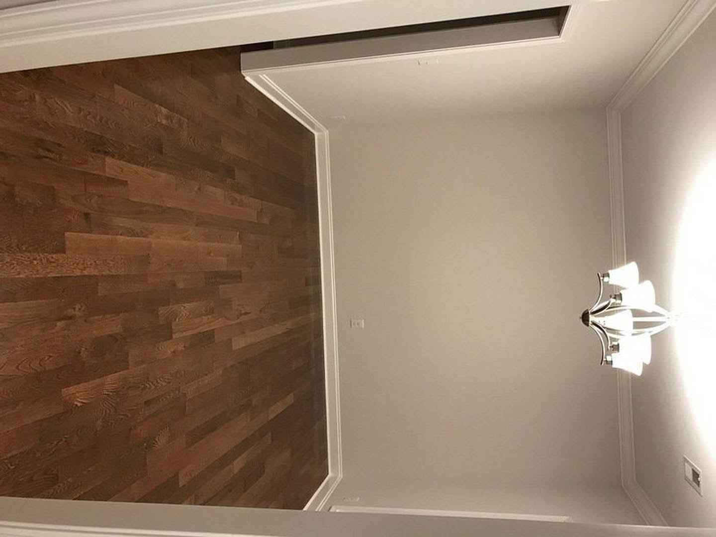 Hallway with warm wood flooring, white trim, and a modern light fixture suspended from a plaster ceiling