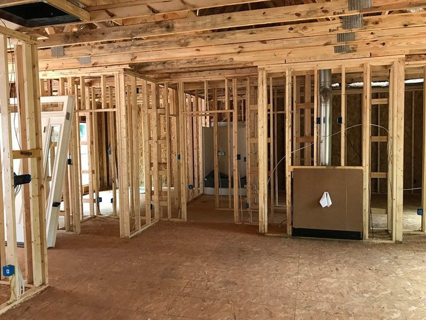 Exposed wood framing and ceiling beams in a partially constructed room with unfinished wooden floor, visible insulation, and several windows.