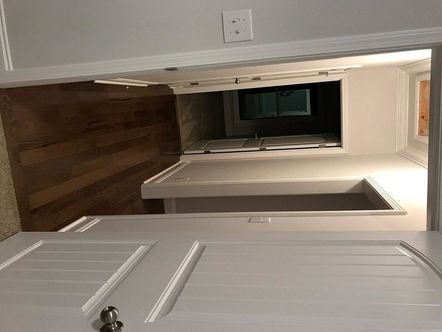 White door with square opening leading to kitchen featuring white cabinetry, stainless steel sink, and light switch on adjacent wall