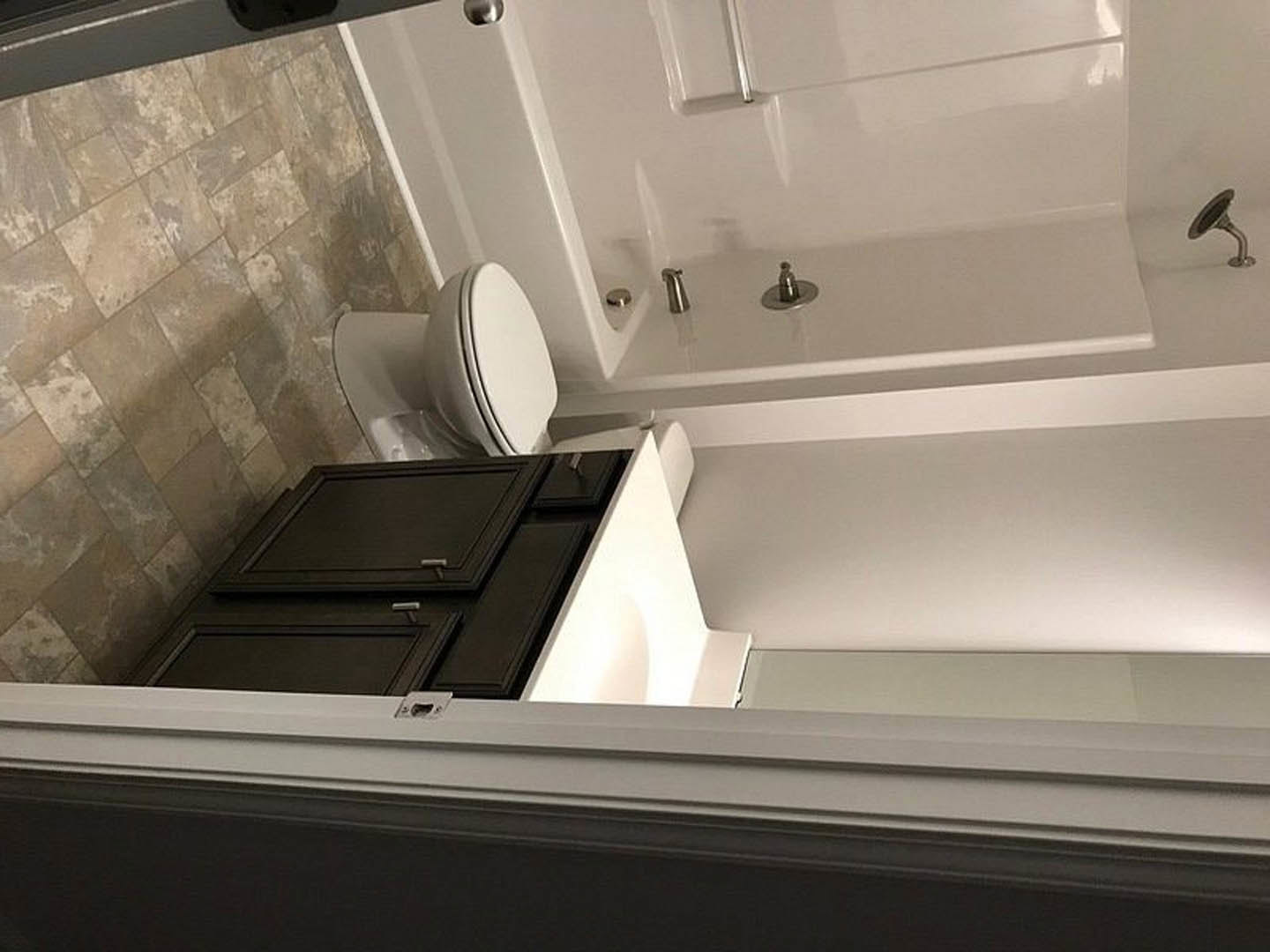 Modern bathroom featuring a freestanding bathtub with chrome faucets, glass-enclosed shower, black vanity cabinet with metal handle, wall-mounted mirror, and tiled walls.