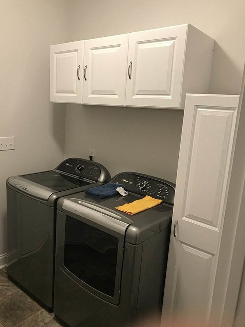 Front-loading washer and dryer set in a laundry room with white cabinetry, towel folded on top, nearby light switch, and black countertop with a small yellow item.