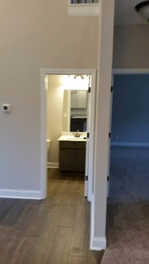 White bathroom with rectangular sink, frameless mirror, light-colored laminate flooring, plaster walls, and recessed ceiling lighting