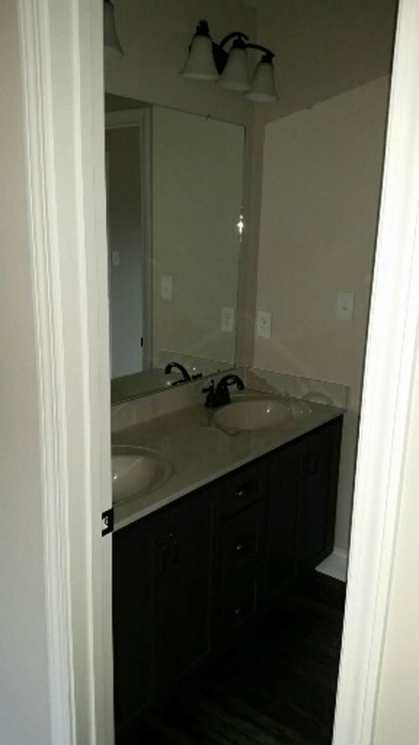Modern bathroom with rectangular mirror above white countertop and undermount sink, chrome faucet, three-light fixture, light gray tile backsplash, and white cabinetry