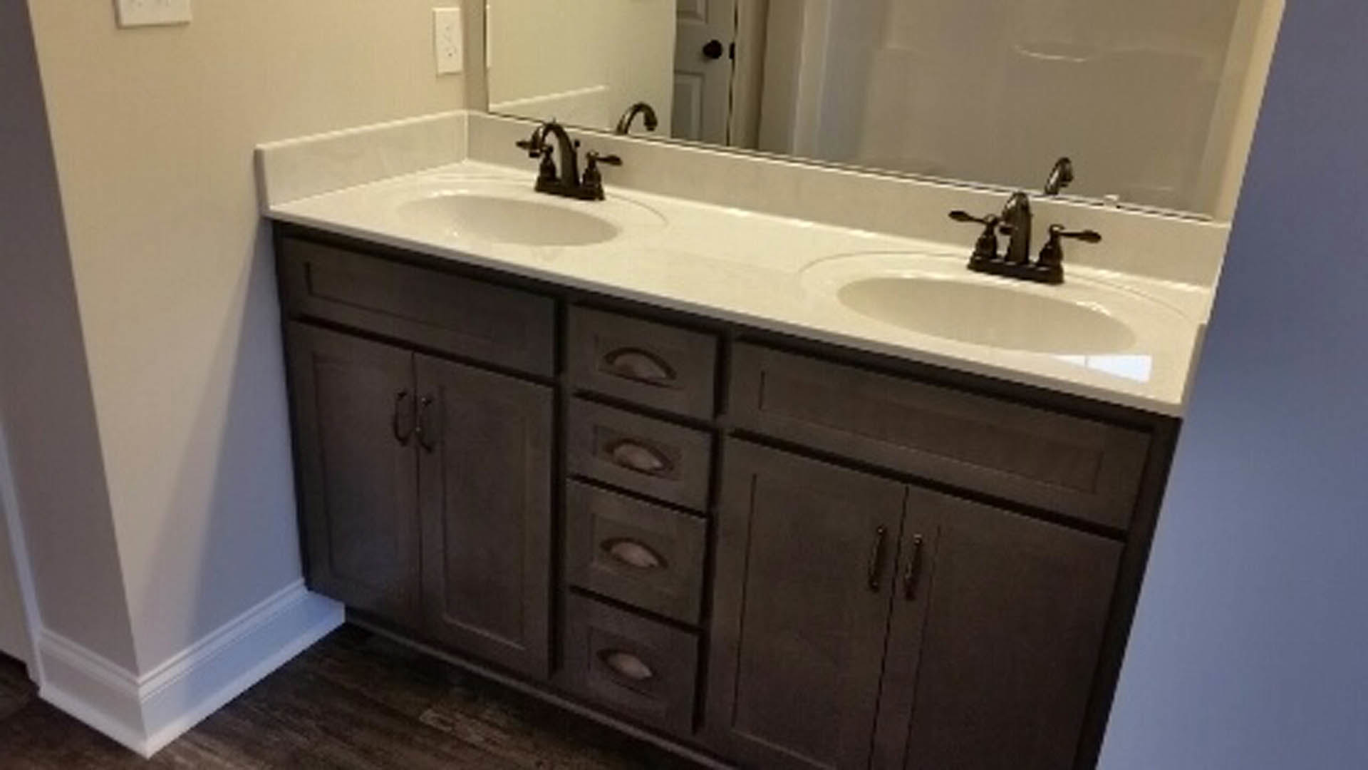 Double vanity with white countertop, two sinks, chrome faucets, large wall mirror, light gray tile backsplash, white cabinetry with drawers, and soft natural lighting.