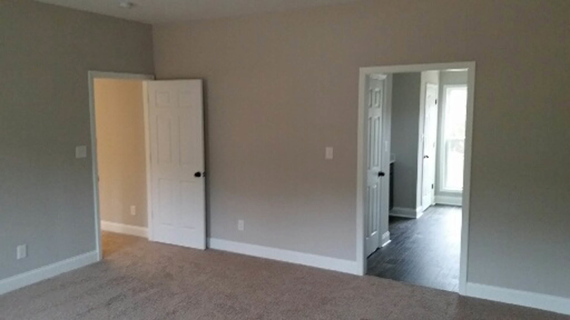 Open white door leading from a light-colored room into a hallway with wood flooring and smooth plaster walls