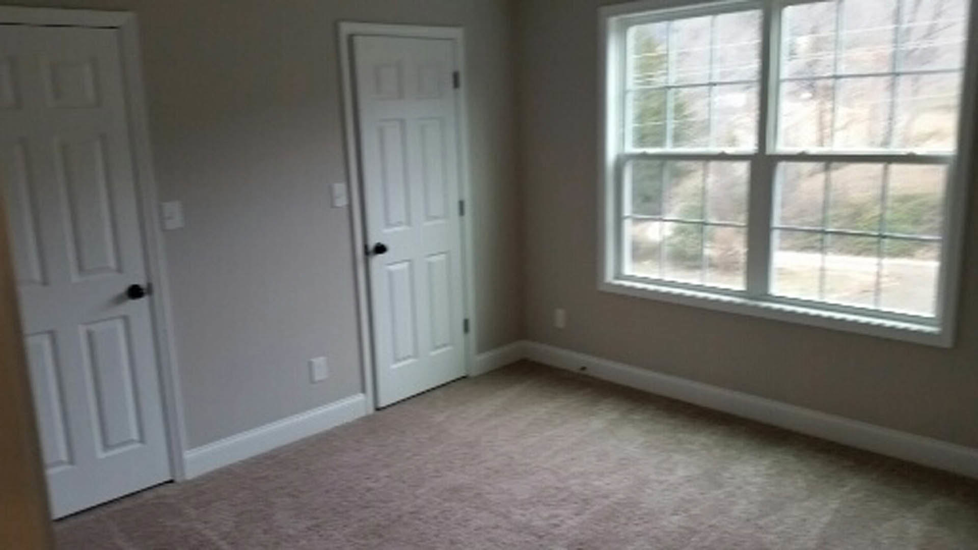 Bright room with light wood flooring, white walls, single-pane window, and paneled door with brushed metal handle
