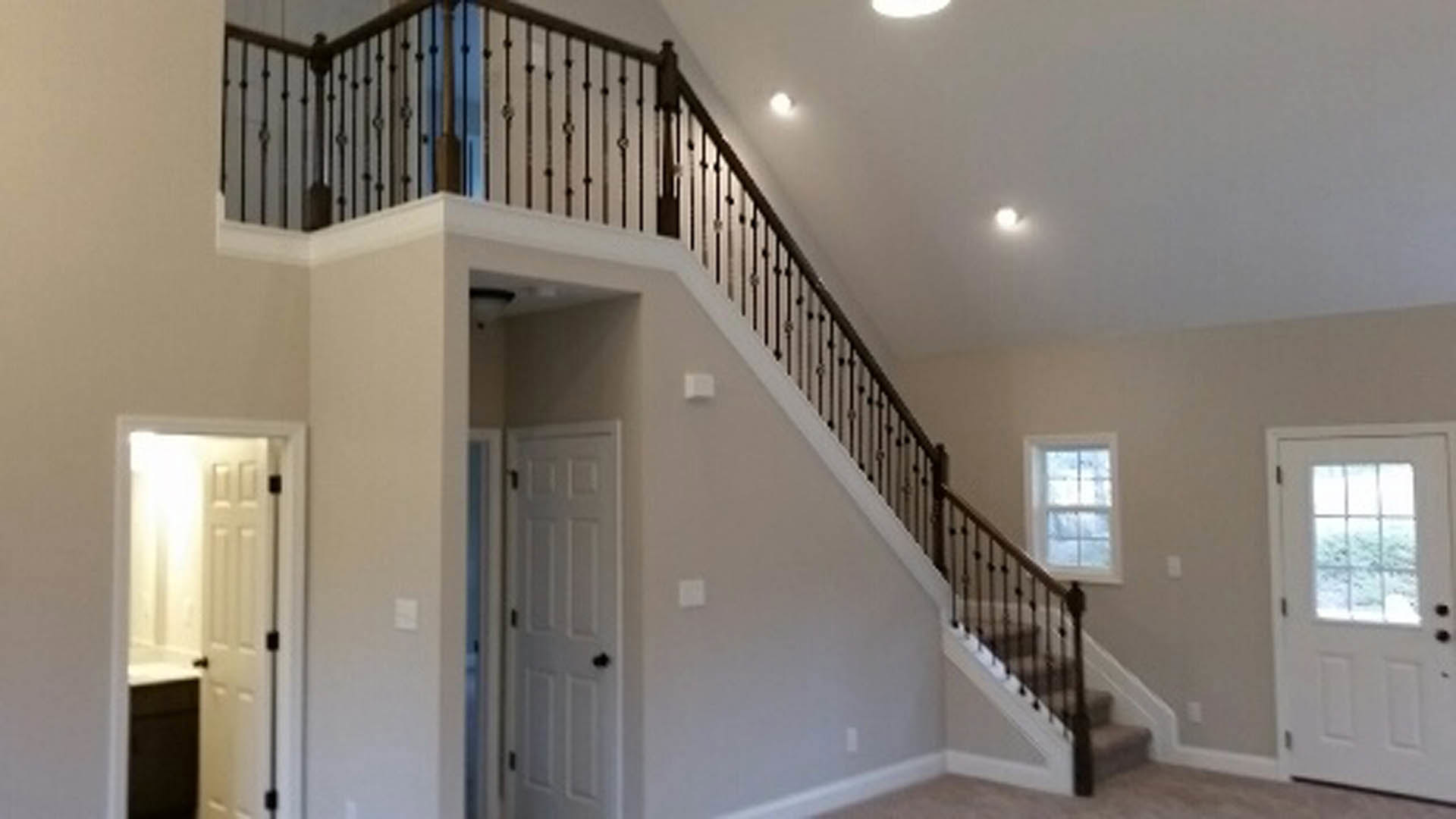 Wood staircase with white balusters and handrail, light-colored walls, white square thermostat on wall, hardwood floor, doorway with molding