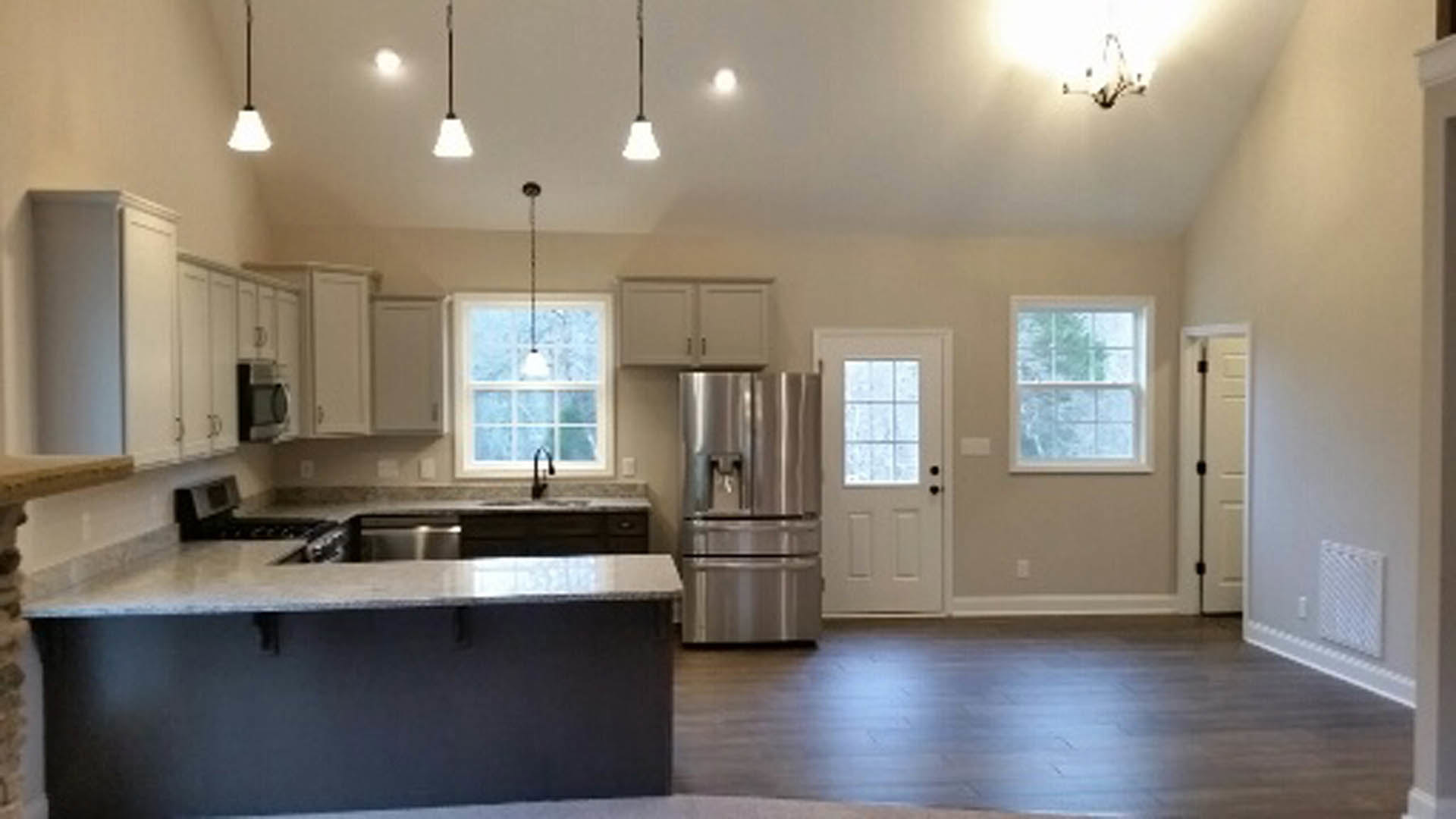 Spacious kitchen featuring a large central island with stone countertop, stainless steel refrigerator, white cabinetry, and wood flooring