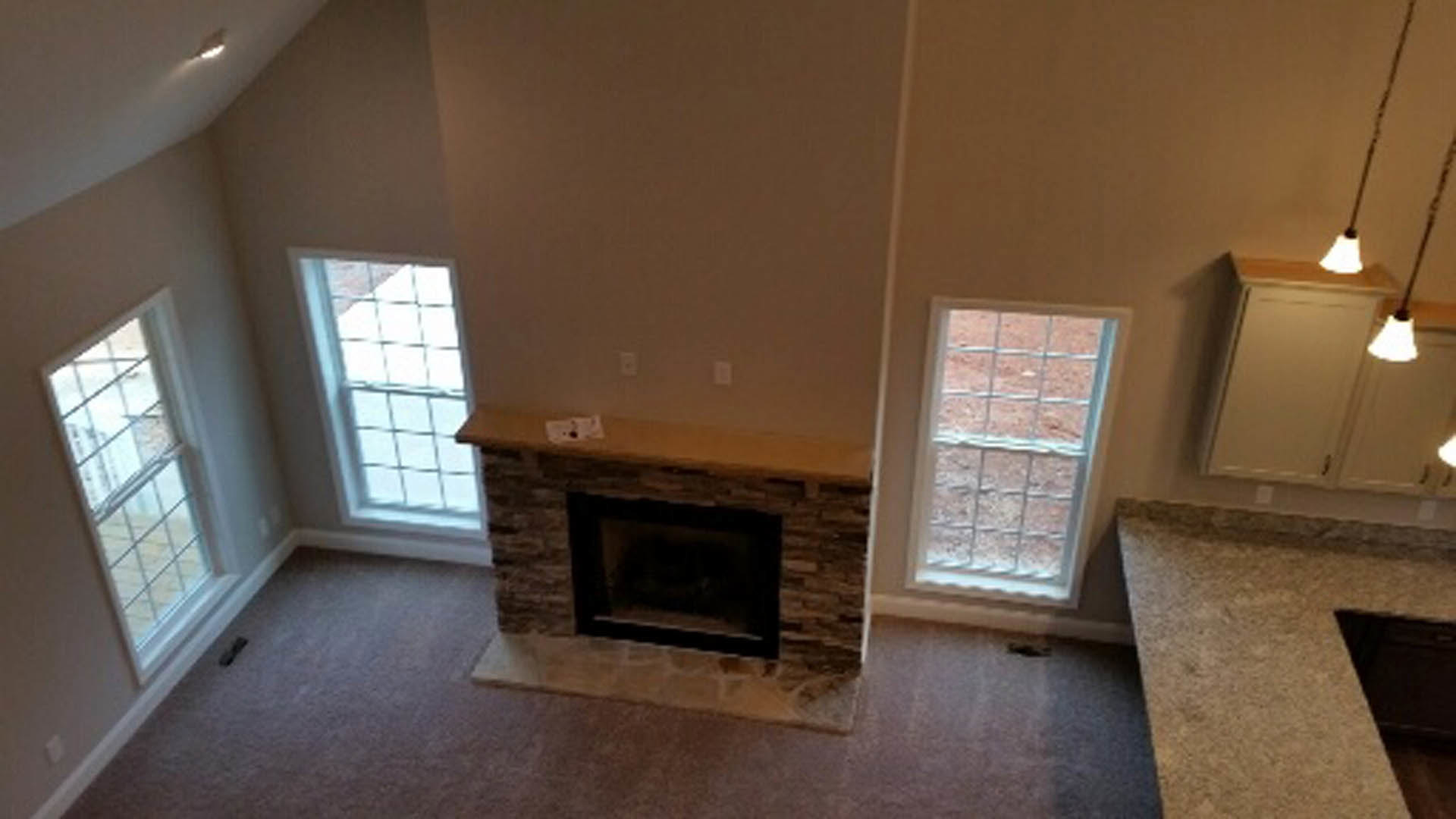 Stone fireplace with white mantel, large windows with trim, hardwood floors, neutral walls, recessed ceiling lights
