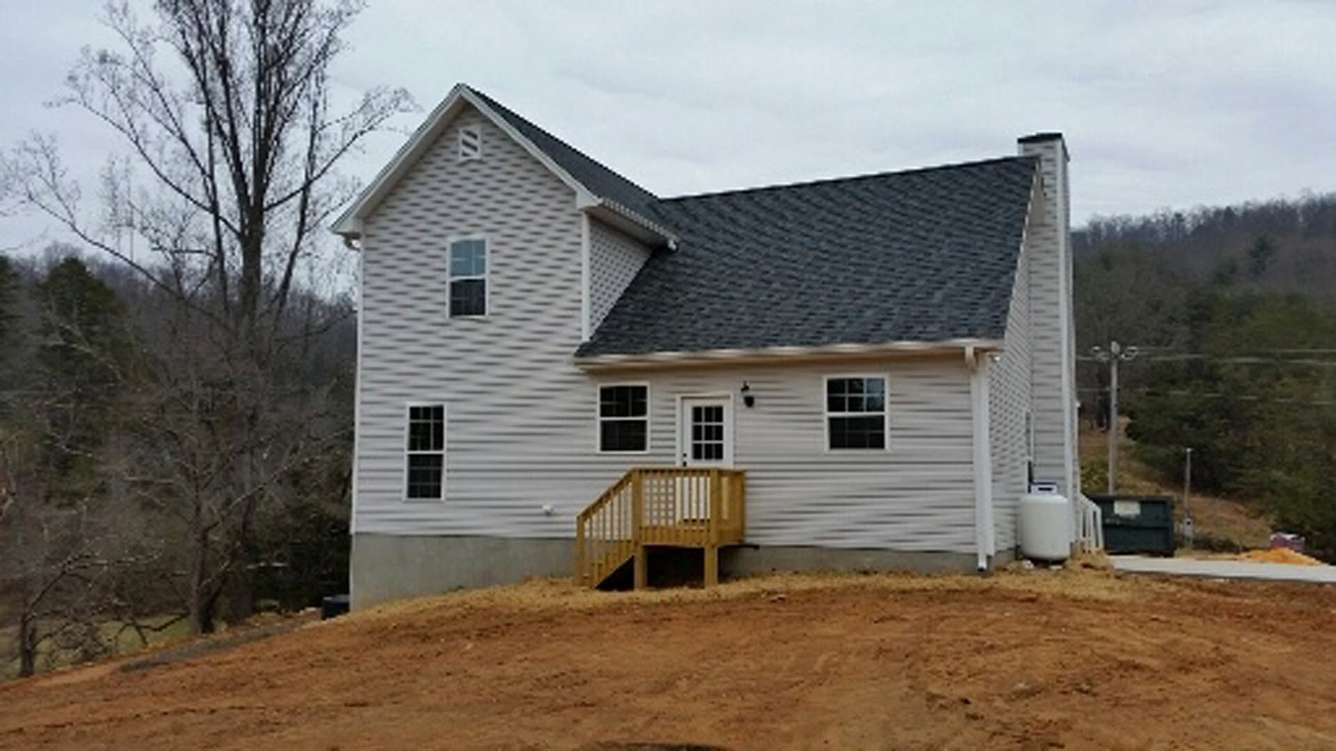 White siding house with covered porch and wooden deck staircase, set beside a dirt hill; trees and Mark Twain Boyhood Home & Museum visible in the background.