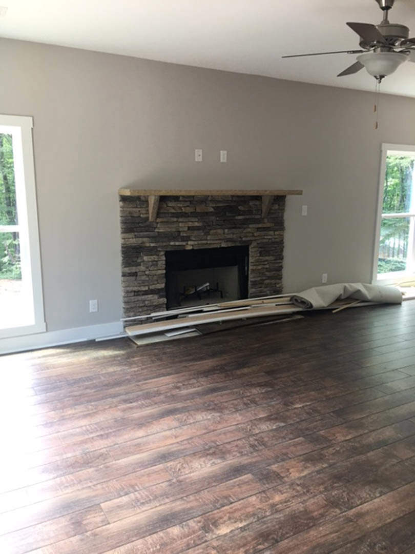 Stone fireplace with fish decor, wood flooring, white-framed window, and ceiling fan with light fixture in a living room