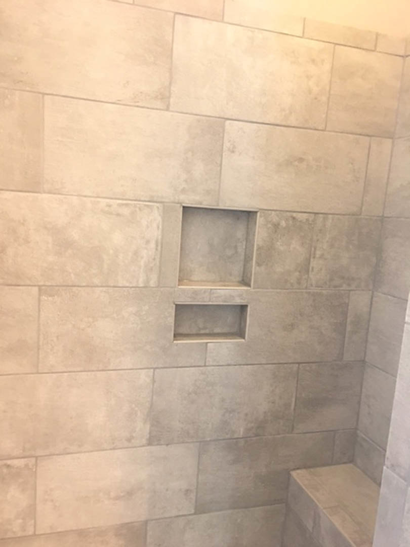 Gray marble tile wall with built-in shelf, white rectangular object resting on gray surface, plaster finish, tile flooring in bathroom interior