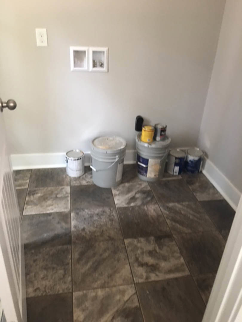 White tile floor with several buckets and cans near a white cabinet with glass doors, yellow container in background, and white electrical outlet on wall.
