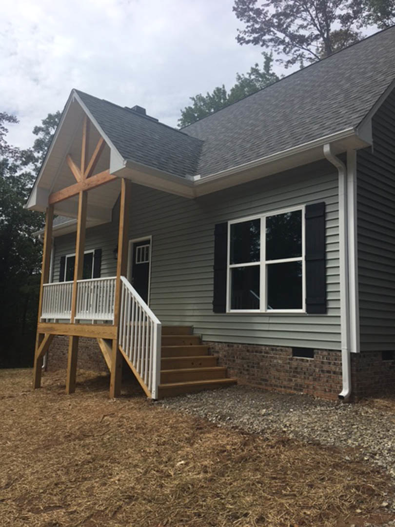 Two-story home with light siding, black shutters, black front door with white trim, covered porch featuring white railing, and staircase leading to entry