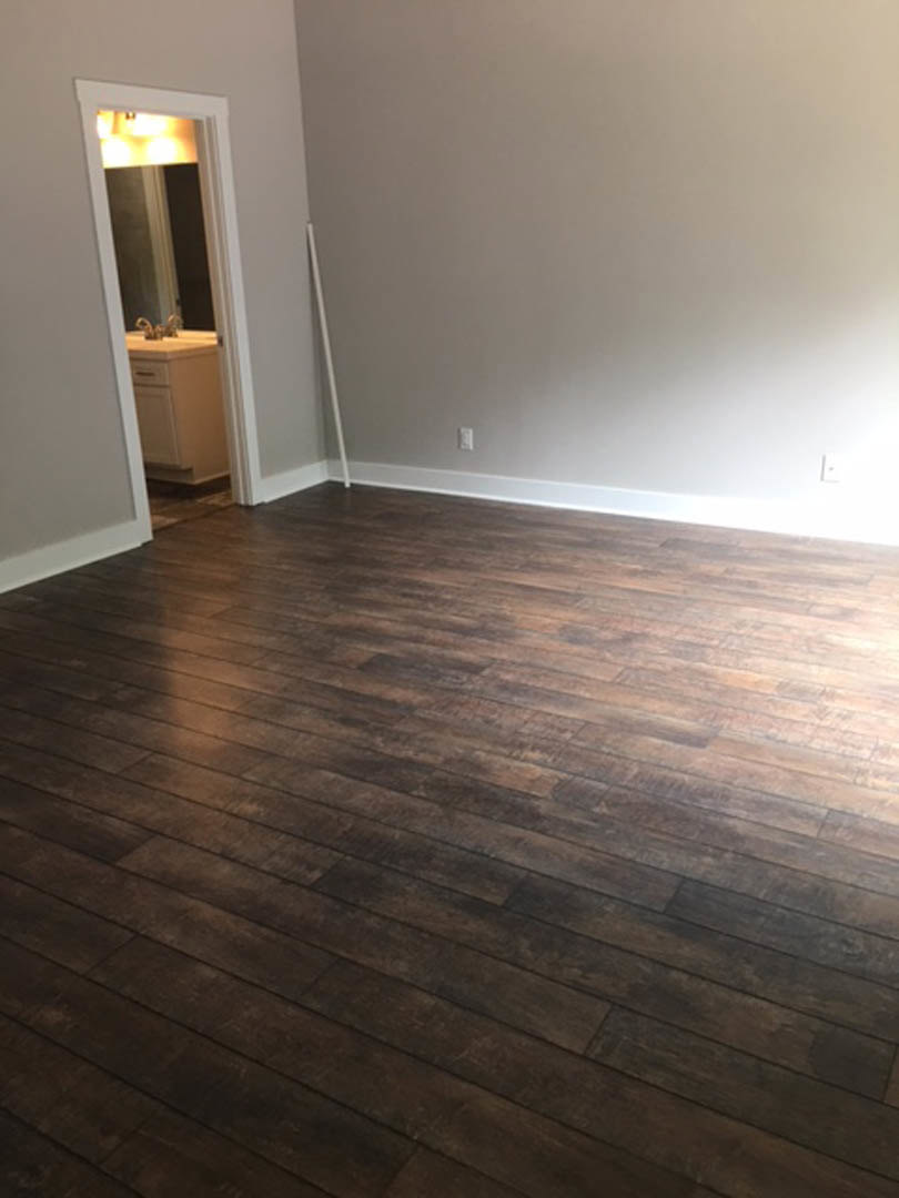 Wood flooring in a room with white walls, white door, and white cabinet topped with a light; mirror and exposed white pipe visible in bathroom area.