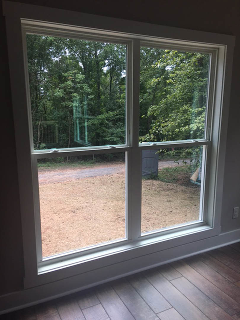 Large window with clear glass overlooking leafy trees, sunlight streaming onto light wood flooring inside a modern home