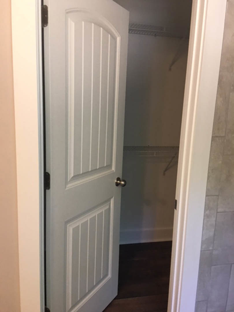 White door with gold knob open to a closet, dark wood flooring, white walls and molding