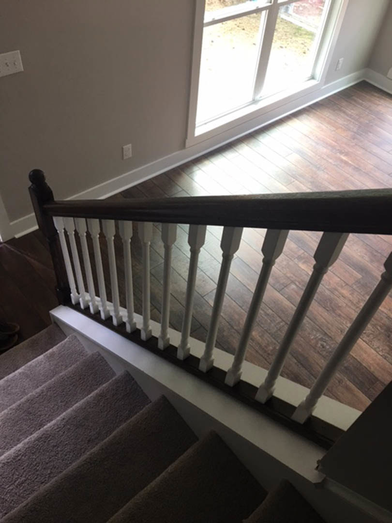 Staircase with white railings and hardwood steps, large window on landing, light switch on adjacent wall