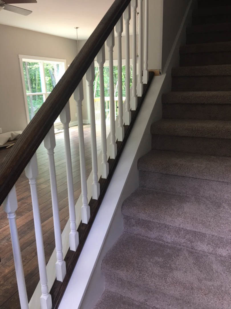 White-painted staircase with matching railing, wood treads, and a large window revealing leafy trees outside