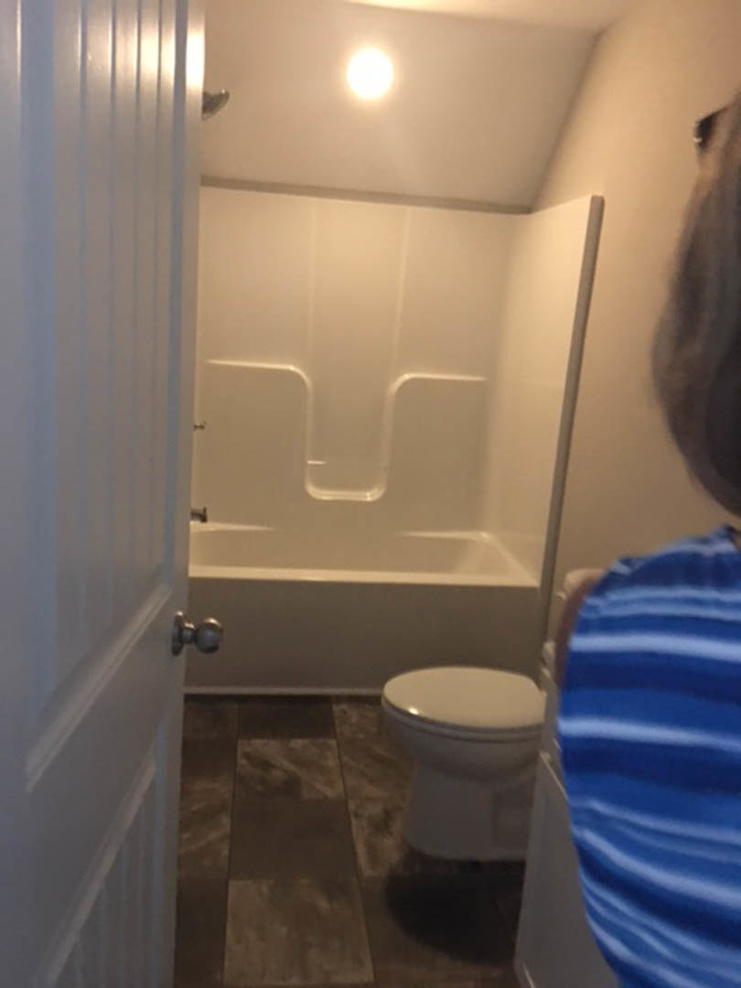 White toilet and bathtub in a bathroom with light-colored tile floor and walls, blue and white striped fabric visible, overall image slightly blurry.