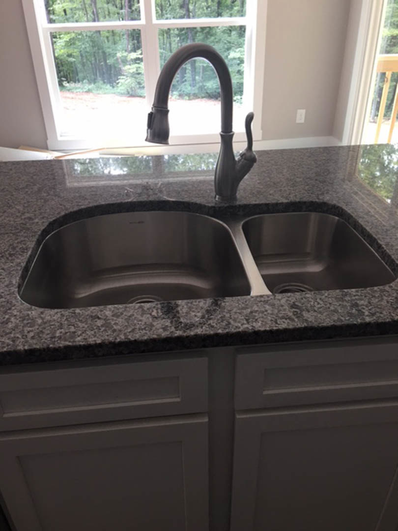 Stainless steel sink with modern chrome faucet set in quartz countertop, white cabinetry below, large window above letting in natural light