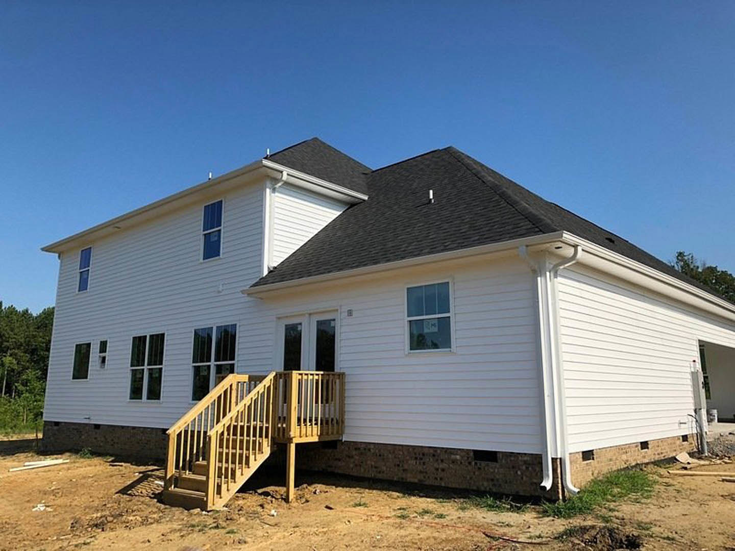 Wooden staircase leading to porch, blue front door, white-framed windows, light siding, tree partially visible in foreground