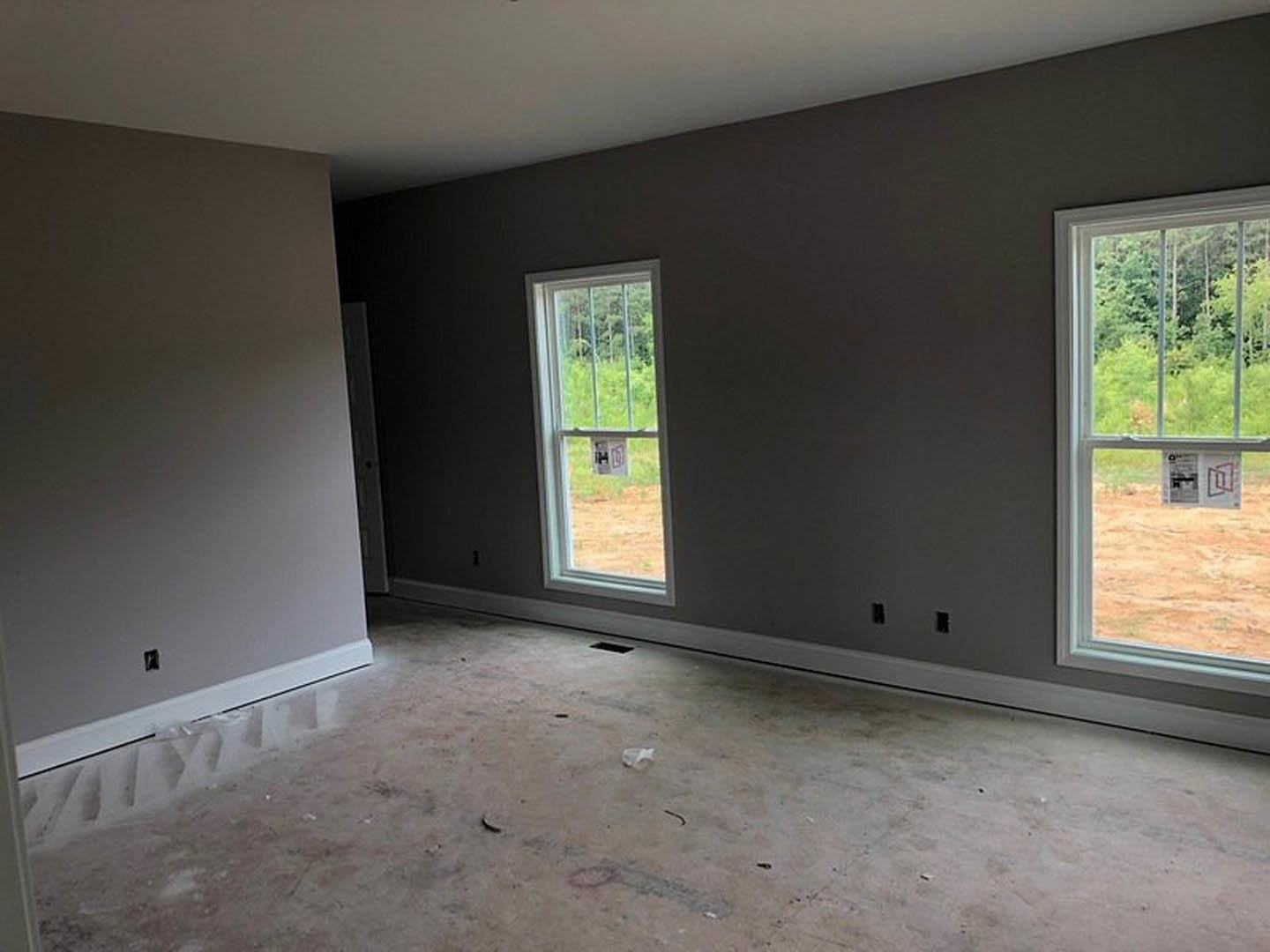 Spacious room featuring large windows, smooth concrete flooring, white plaster walls, and natural daylight streaming in.