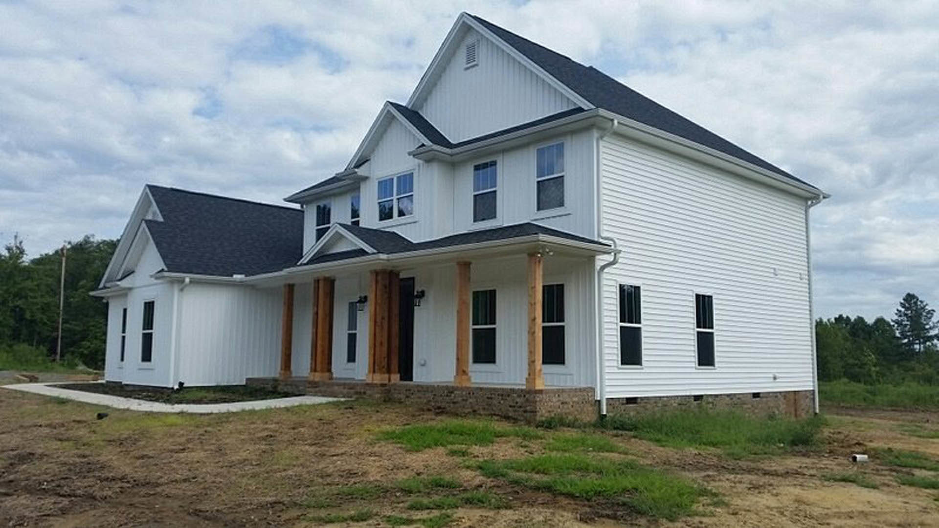 White two-story house with tall white pillars, wide windows with white frames, expansive green lawn, and a porch; blurred dog visible in foreground grass.