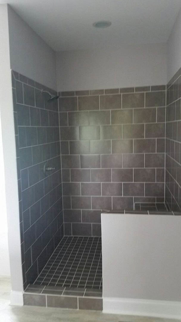 Shower with grey tile walls and black tile floor, white bathtub, linear drain, white plaster wall