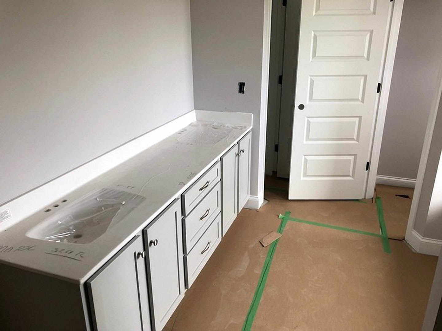 Brown countertop with built-in sink and drawers, white door with black knob, green tape on wood floor, plastic bag near sink, close-up of toothbrush on counter
