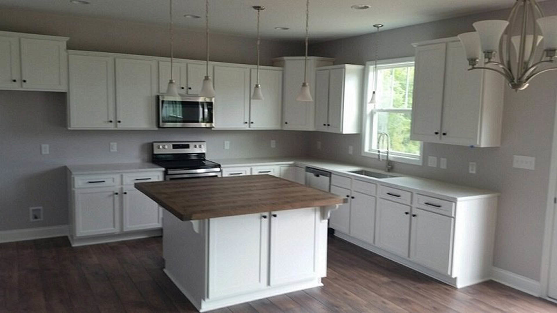 White kitchen cabinets, wooden island with wood countertop, stainless steel appliances, light fixtures overhead, hardwood flooring