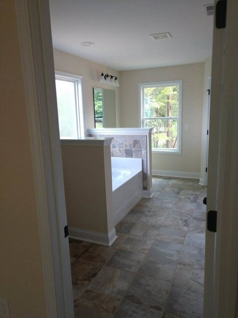Freestanding bathtub beside a large window with tree views, light gray tile flooring, white plaster walls, and modern light fixture