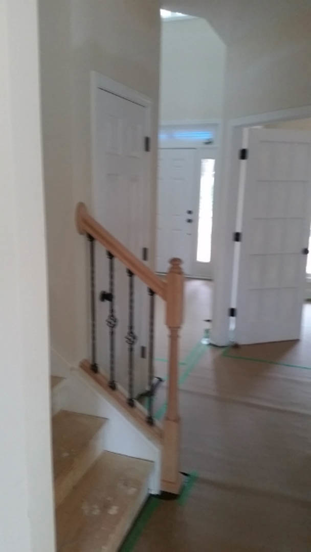 Wood staircase with white risers and dark handrail, white door with black hardware, light plaster walls, hardwood flooring