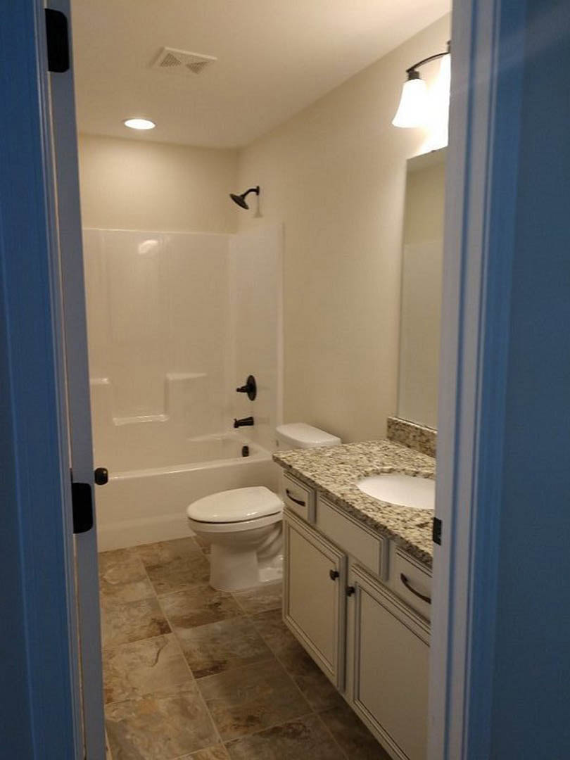 Marble countertop with undermount sink, white toilet with closed lid, bell-shaped light fixture, tile flooring, wall vent, chrome faucet