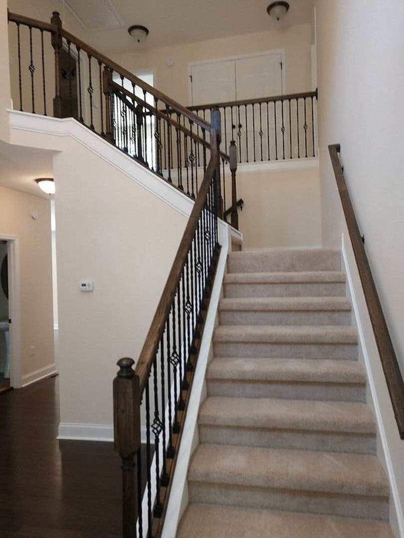 Dark wood staircase with sleek metal railing, white baseboards, and adjacent white cabinet on polished flooring