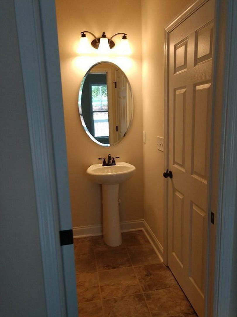 White pedestal sink with chrome faucet beneath rectangular wall mirror, surrounded by light gray tile floor and white walls in bathroom.