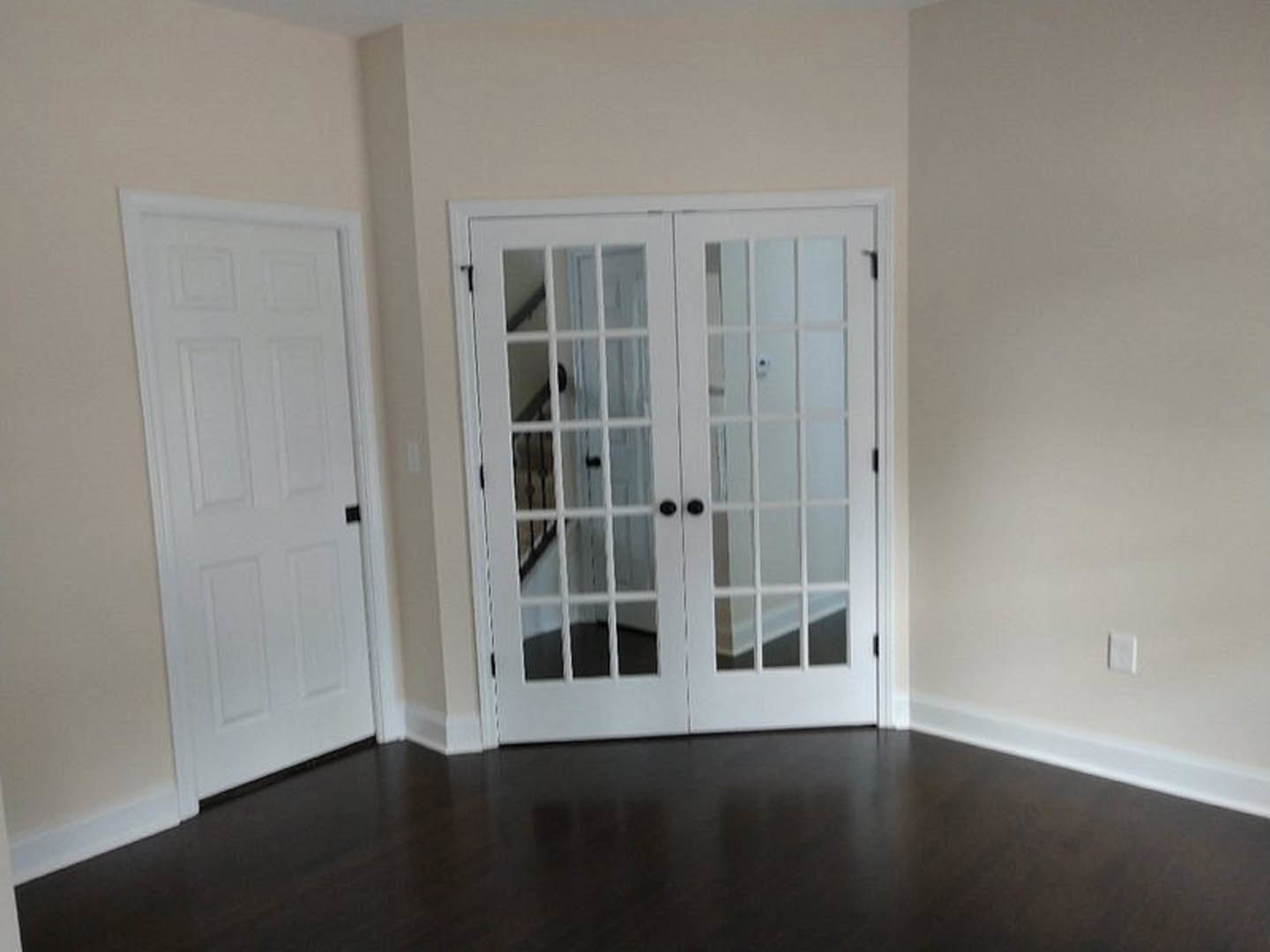 White paneled doors with black handles, dark polished wood flooring, white walls, and a white light switch