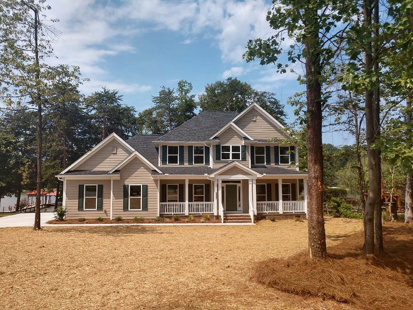 Two-story house with white siding, covered front porch, large green lawn, mature tree in foreground, white-framed windows, cloudy sky overhead