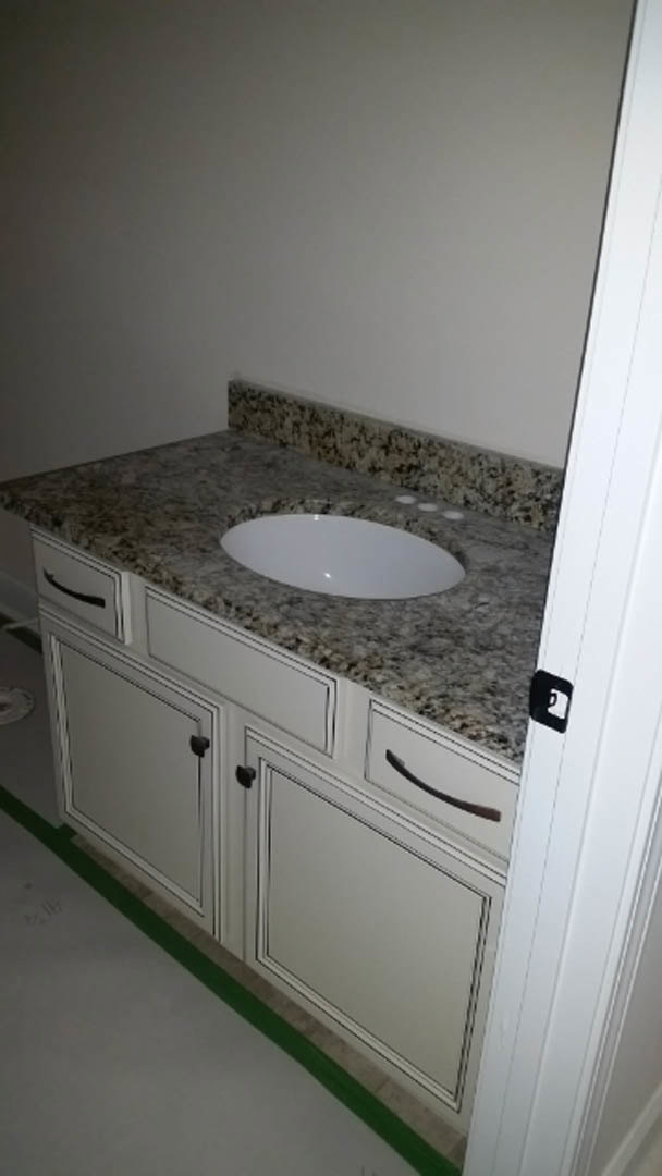 Rectangular undermount sink set in a light stone countertop, chrome faucet, white tile backsplash, wood cabinetry, and partial view of bathtub in modern bathroom.