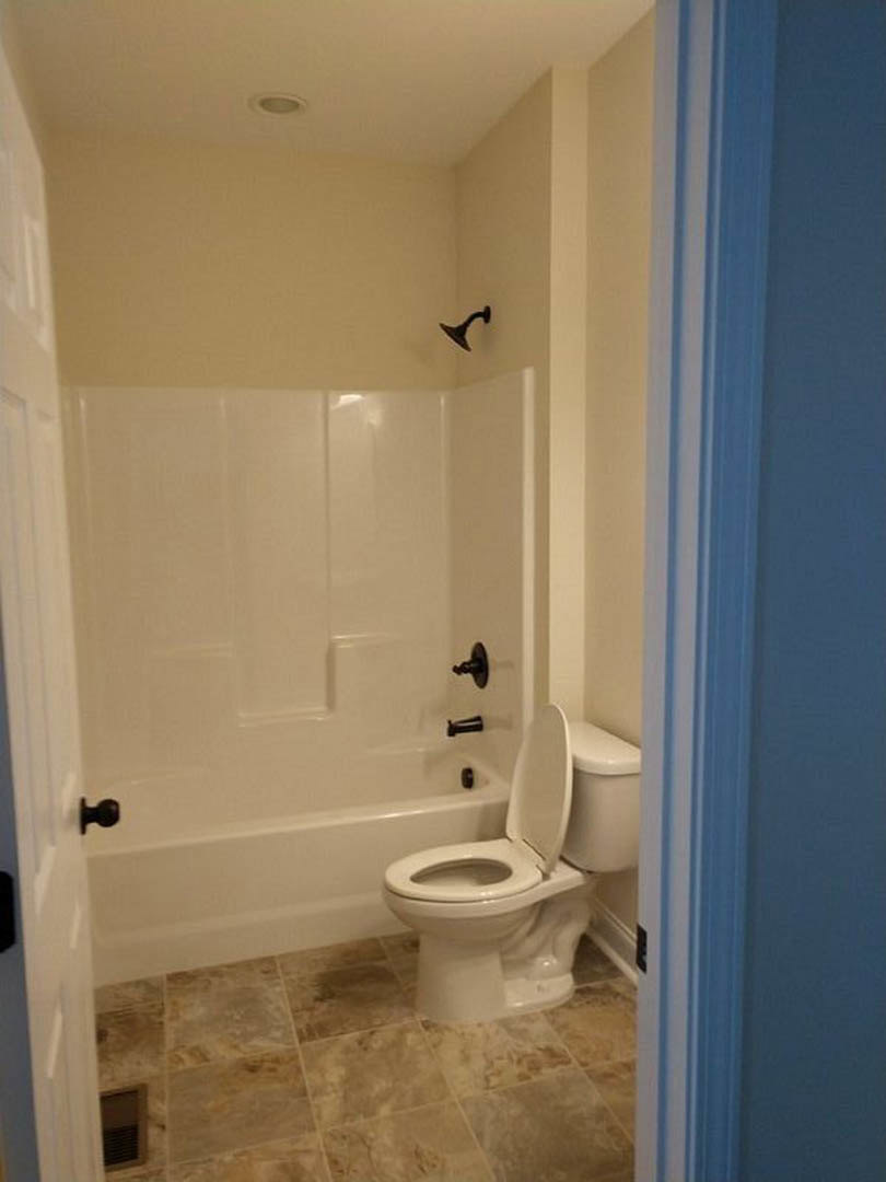 Modern bathroom featuring white toilet with seat up, glass-enclosed shower, light gray tile walls, and chrome plumbing fixtures