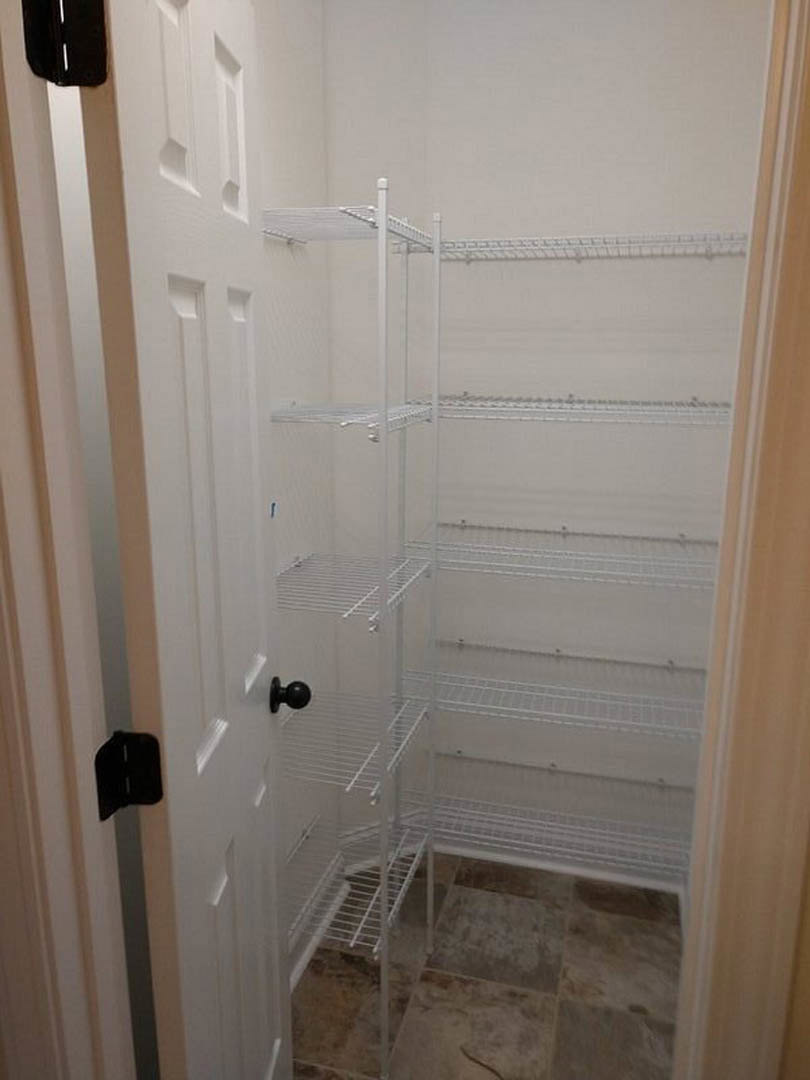 White closet with built-in shelves, smooth plaster walls, and a black bag resting on a shelf.
