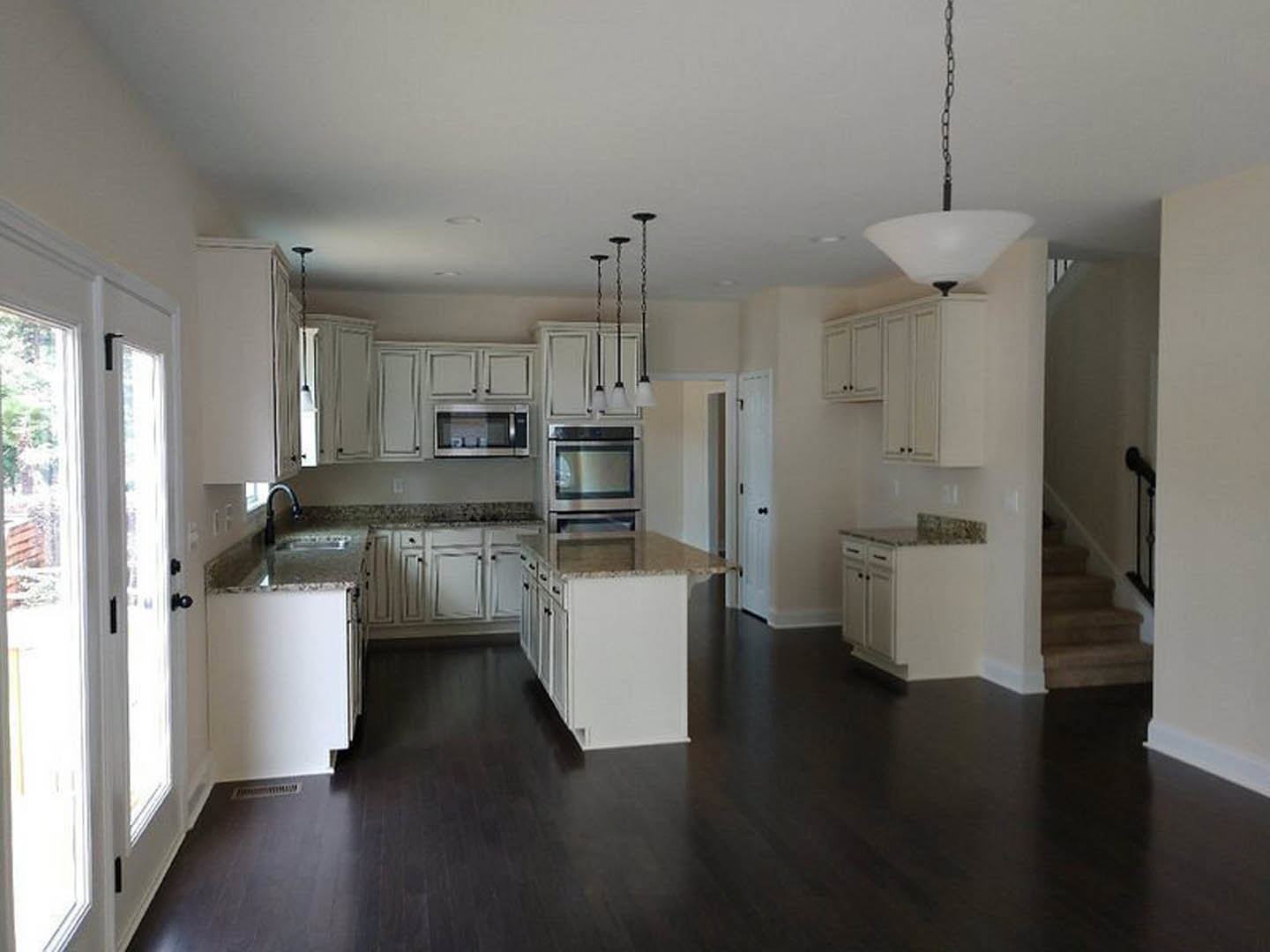 White kitchen cabinets with marble countertops, stainless steel appliances, dark hardwood flooring, and a modern light fixture