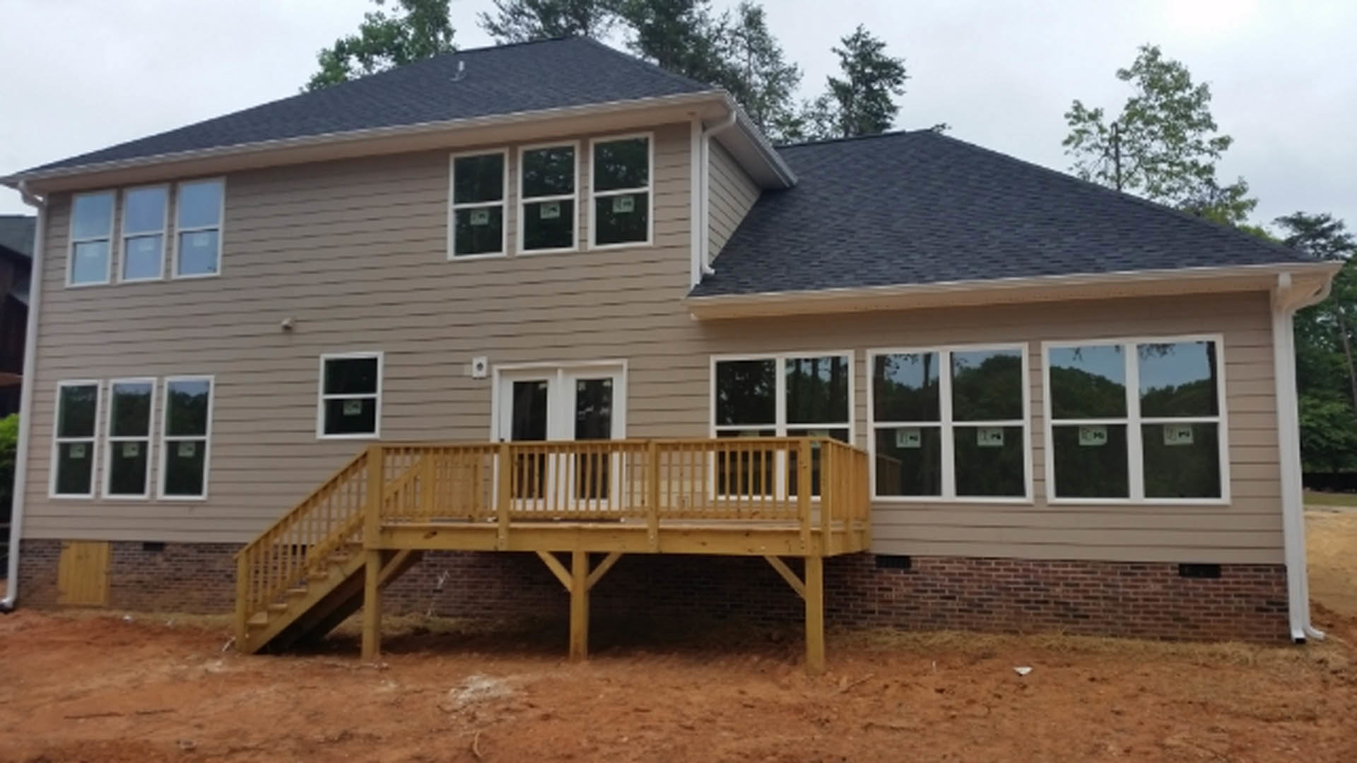 Two-story home with light siding, covered front porch, wooden deck with railing, large windows, and landscaped yard