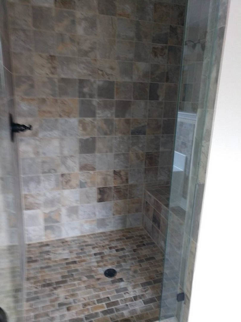 Walk-in shower with clear glass door, tiled walls and floor, linear drain, adjacent white paneled door, partial view of window and decorative bird motif