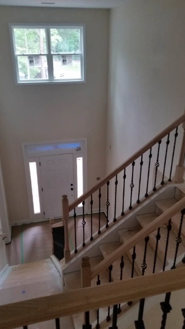 Wood staircase with white balusters and handrail, adjacent to a white door with glass window, large window revealing leafy trees outside, light-colored walls and flooring