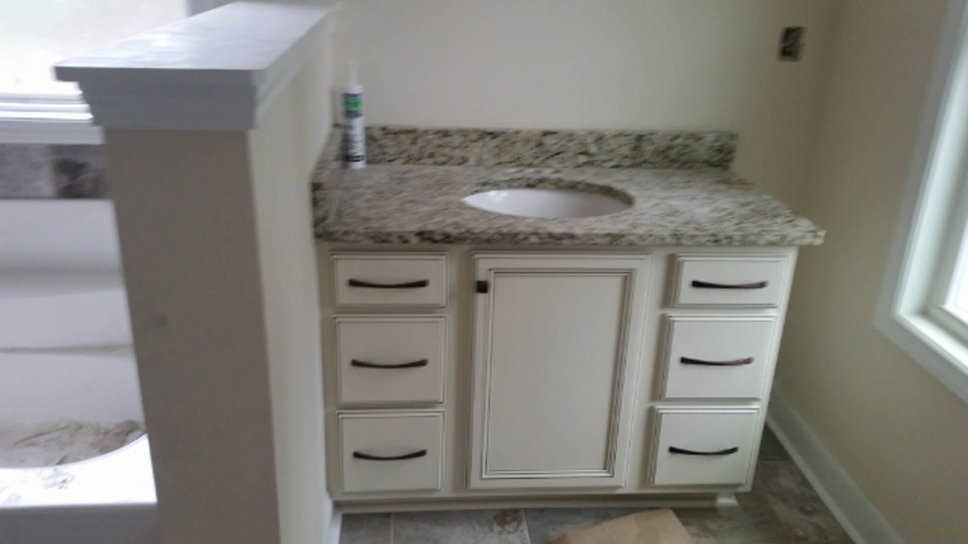 Bathroom featuring a marble countertop with an undermount sink, dark cabinetry drawers, white door with black handle, and light tile flooring.