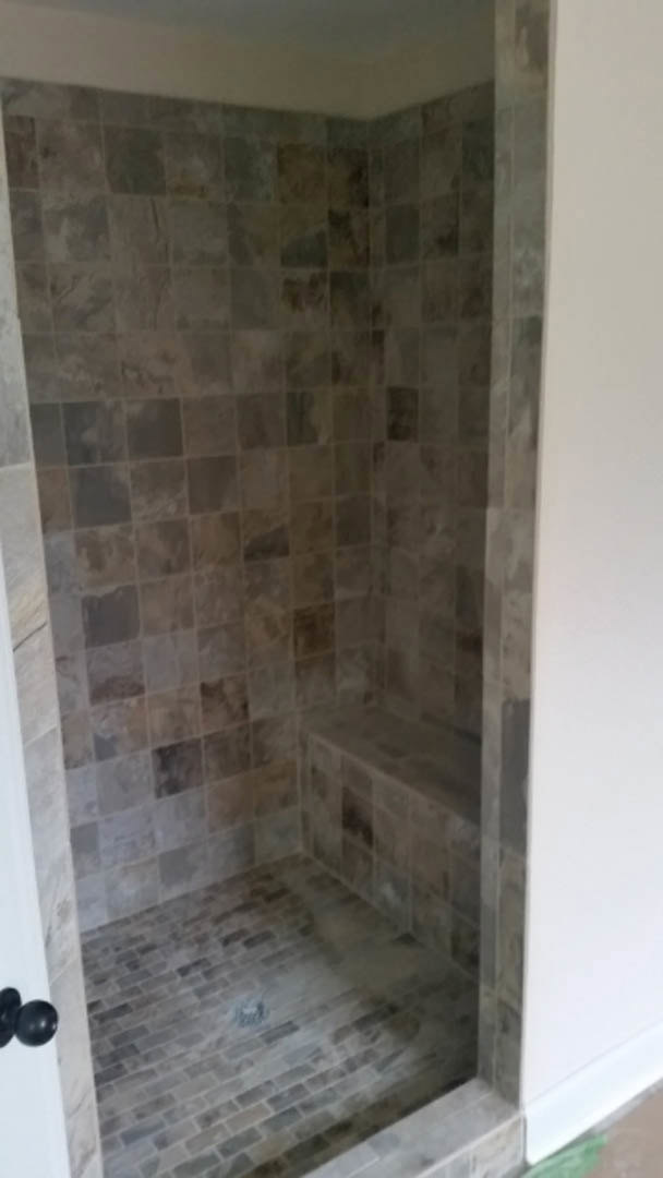 Walk-in shower with marble tile walls, built-in bench, glass door, and grey tile flooring